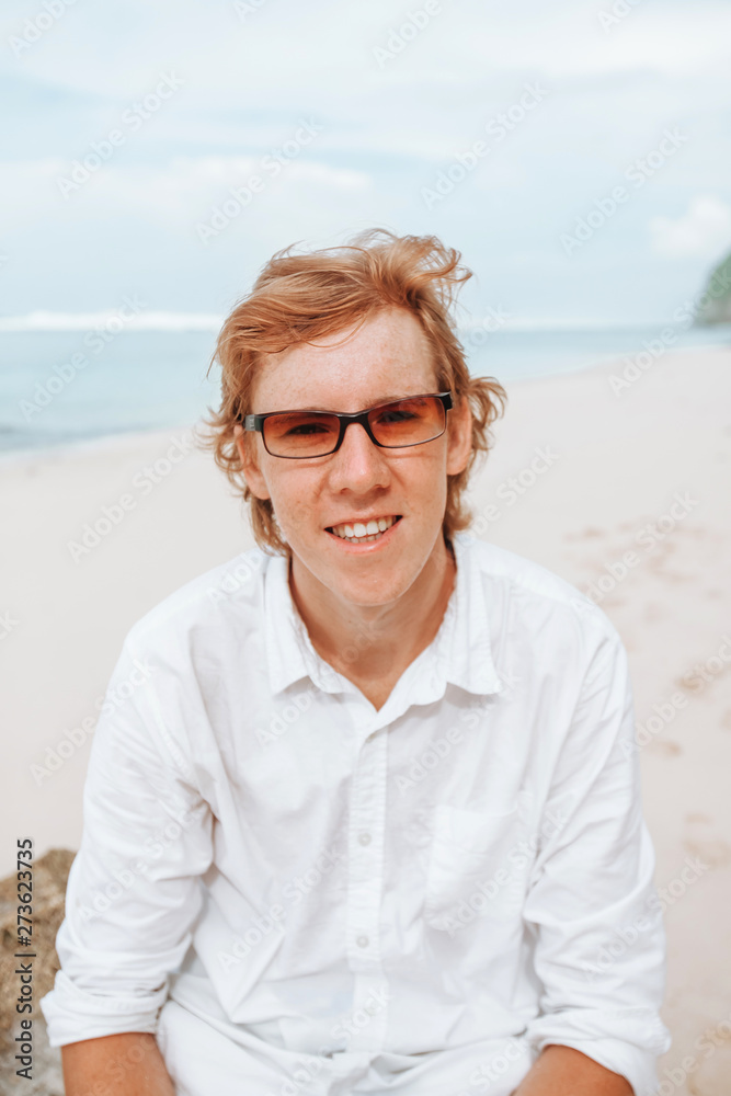 Portrait of a red-haired man in white clothes on a white beach in sunglasses