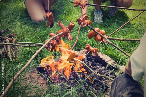 BBQ sausages on sticks. A bunch of friends roasts sausages over an open fire.Tourist and camping concept. Toasting strong sausages over open fire in nature.