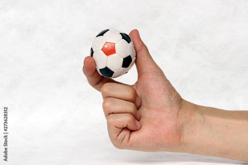 Fototapeta premium Mini ball of football in hand and one black point of football is China flag, hold it with two finger on white background.