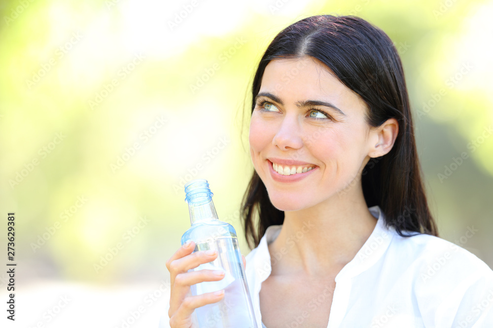 Happy woman holding a bottle of water looking at side Happy woman holding a bottle of water looking at side