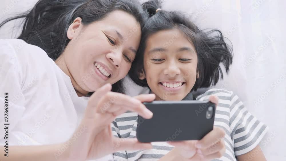 Mom and daughter are watching funny clips together. Asian women and girl are cute, fun and happy on the bed Mom and daughter are watching funny clips together. Asian women and girl are cute, fun and happy on the bed