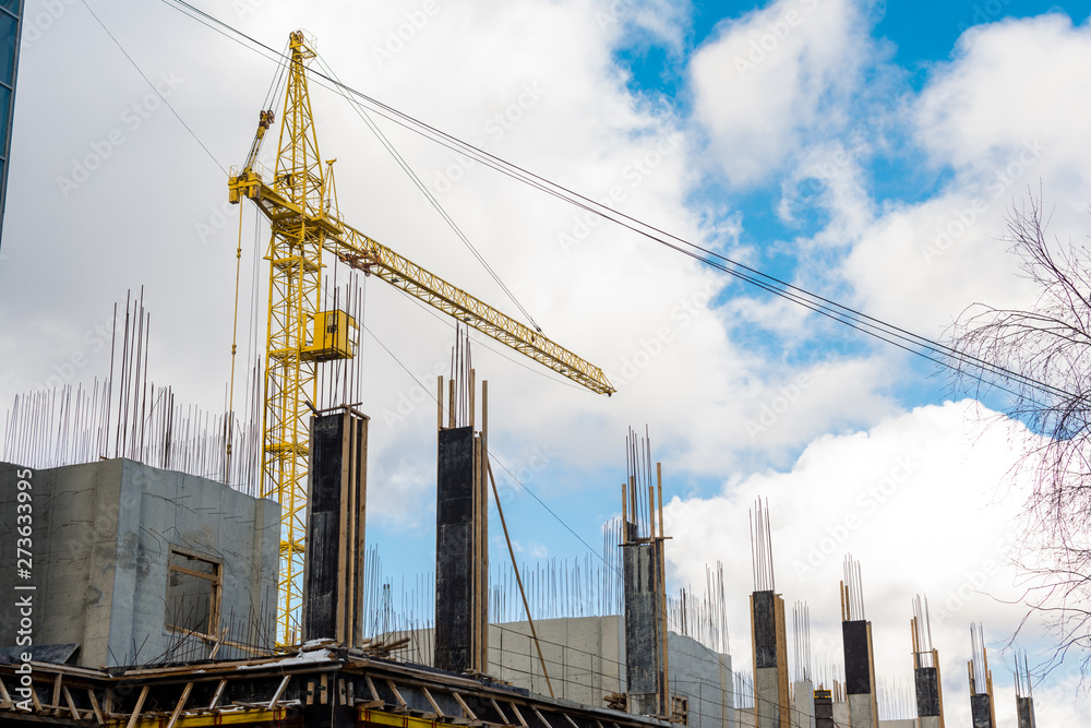 The process of building a multi-storey residential building, a yellow tower crane, poured concrete columns with fittings against a blue sky with clouds