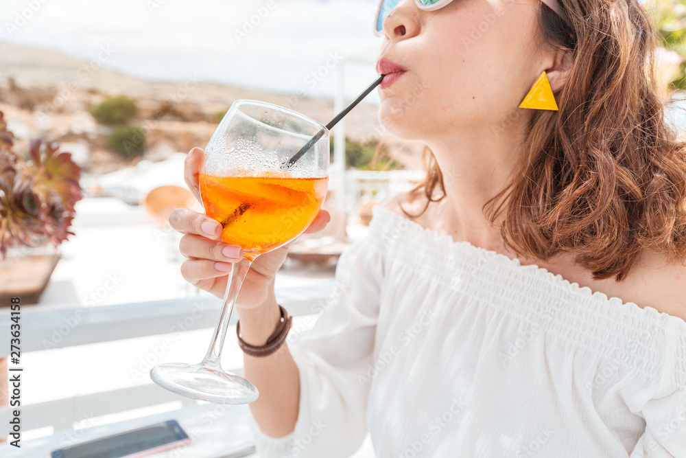 Fototapeta premium Happy asian woman enjoying aperol spritz cocktail in a greek cafe. Beverage and refreshment concept