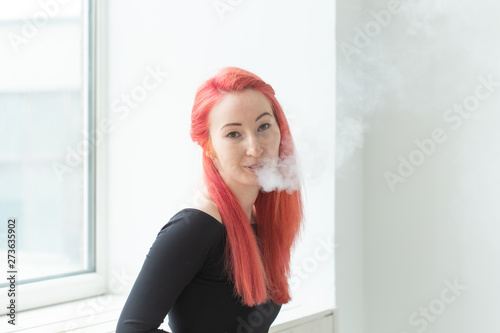 Vape  addiction and people concept - young woman with colored hair is smoking a vape