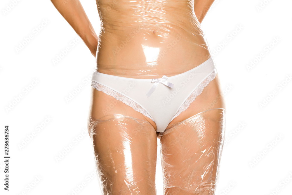 woman wraps her legs and belly with plastic foil on white background - obrazy, fototapety, plakaty 