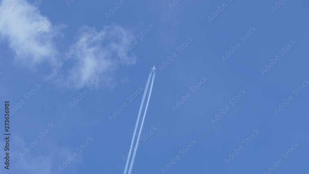 the plane flies across the blue sky and leaves a trail