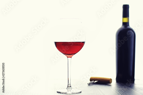 A glass of red dry wine on the table. Dark bottle and glass of wine.