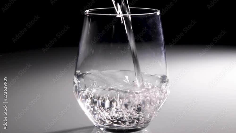 Water being poured into a clear glass with a dark background. Water being poured into a clear glass with a dark background.
