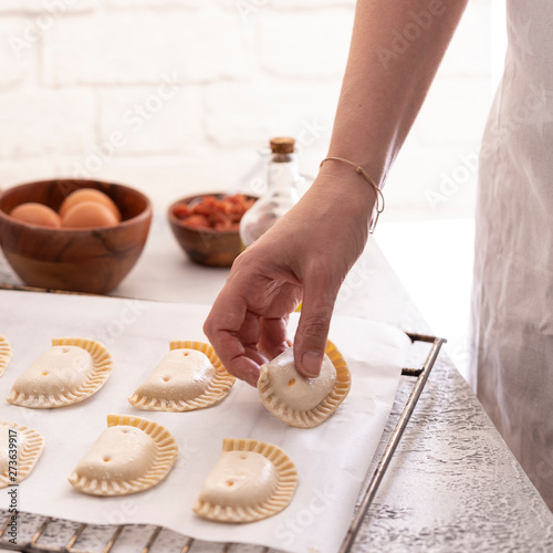Woman put empanadillas , small filling tuna pies in roasting tray to baked pastry in oven. Typical snack in Latin American cultures and Spain. Natural atmosphere lifestyle image.