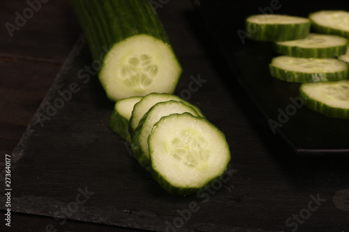 Fresh sliced cucumbers on black cutting board and wood rustic background. Flat lay pattern of green cucumbers on table