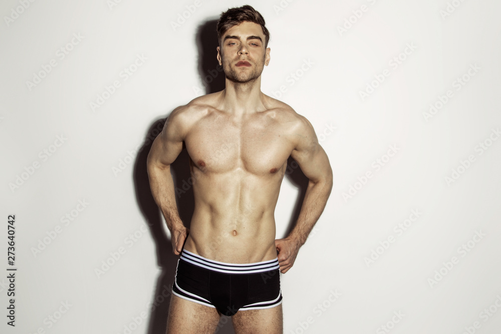 Strong stripped muscle male model in black underwear with white strips on white isolated font background with shadow