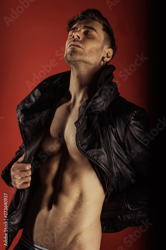 Handsome sport sexy stripped guy portrait in leather jacket on isolated rouge red background