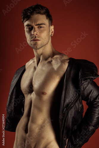 Handsome sport sexy stripped guy portrait in leather jacket on isolated rouge red background