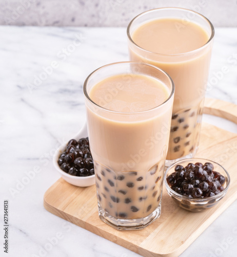 Popular Taiwan drink - Bubble milk tea with tapioca pearl ball in drinking glass on marble white table wooden tray background, close up, copy space