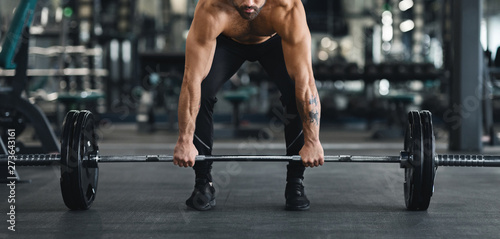 Muscular guy lifting heavy barbell from gym floor