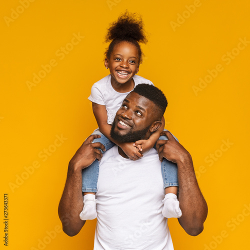 Cheerful black man riding his cute little daughter on shoulders