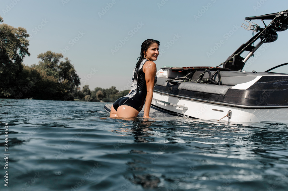 Brunette surfgirl leans on surfboard near boat