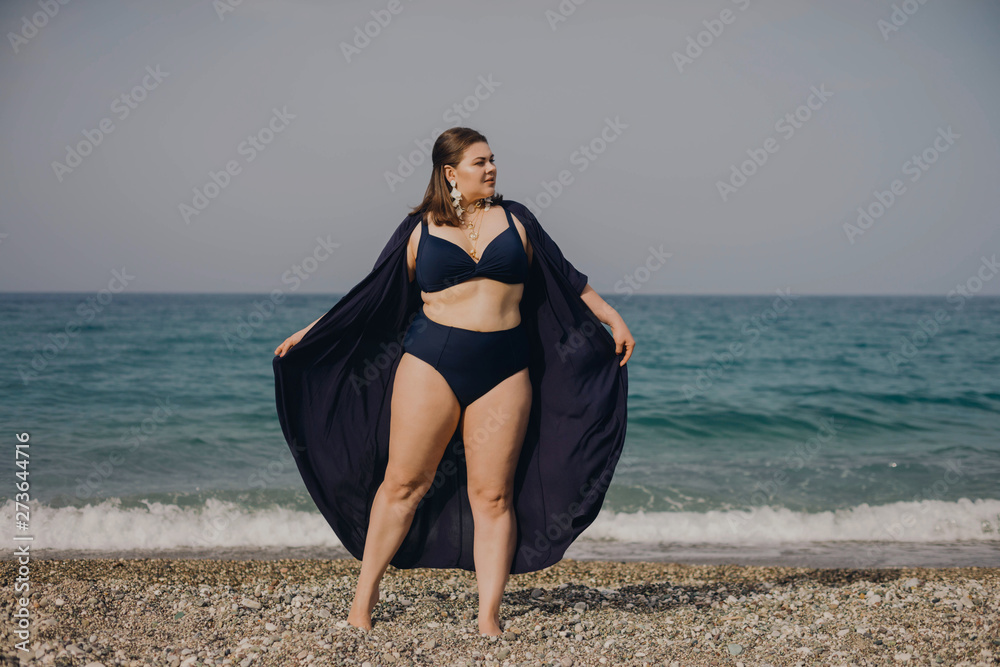 Attractive busty curvy woman in a blue swimsuit resting on the beach.  Stylish accessories, fashion for plus size, beautuful sea. Bodypositive,  natural authentic beauty, resort, summer vacation. Copy Stock Photo | Adobe