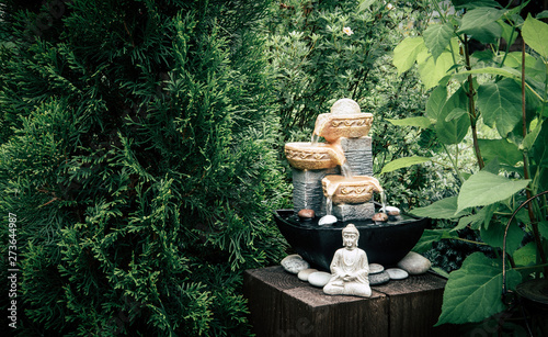 Canvas Print Small home garden private fountain with meditating Buddha statue between trees and bushes