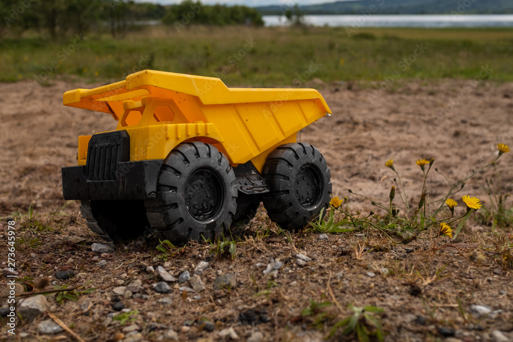 Obraz premium A child's yellow dump truck abandoned on the ground by a lake, side on view