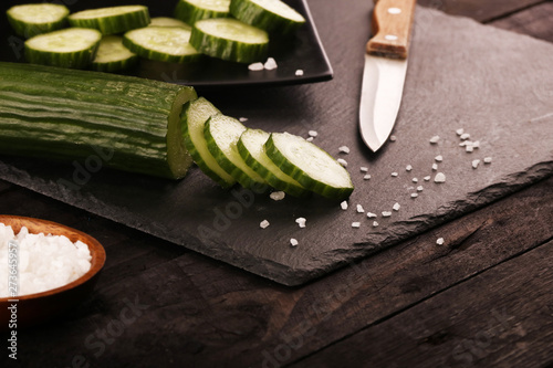 Sliced green cucumbers with knife and salt on black plate and black wood rustic table.