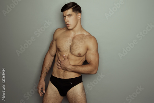 Strong stripped muscle male model in black underwear on grey isolated font background