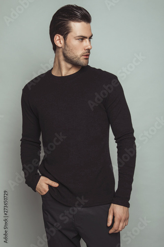 Muscle strong beautiful stripped male model in black jamper and black trousers on grey isolated font background