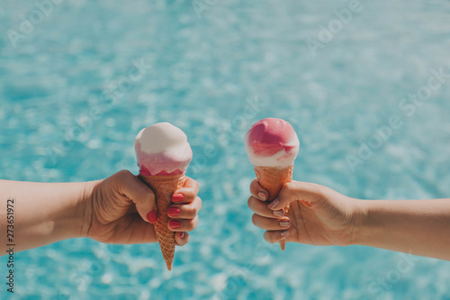 Two friends hold pink ice cream on a hot day on background of a blue pool. Hands with a beautiful manicure, the concept of leisure, summer vacation. Copy space.