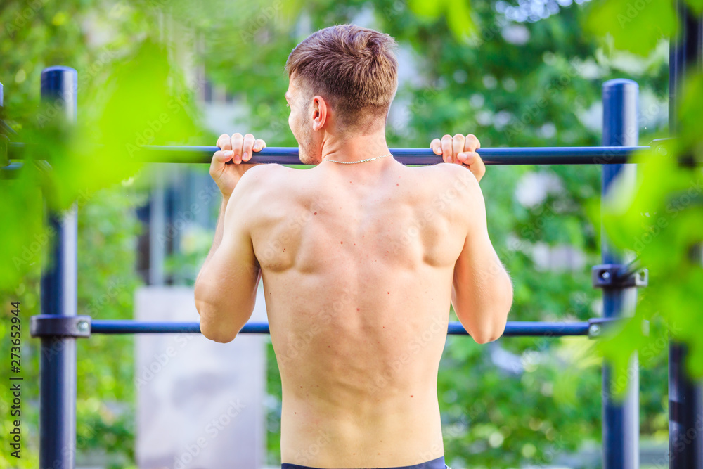 Workout in summer: Young fit Caucasian man is doing pull ups. Naked back.
