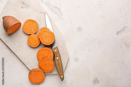 Cutting board and knife with raw sweet potato on light background