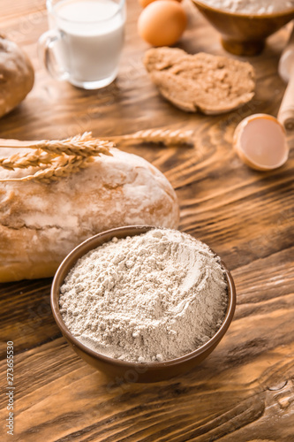 Bowl with flour and bread on wooden table