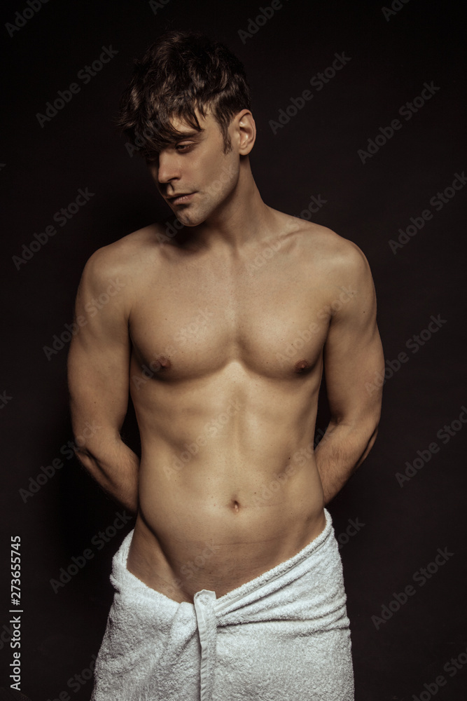 Fototapeta premium Strong stripped muscle male model with white towel on black isolated font background