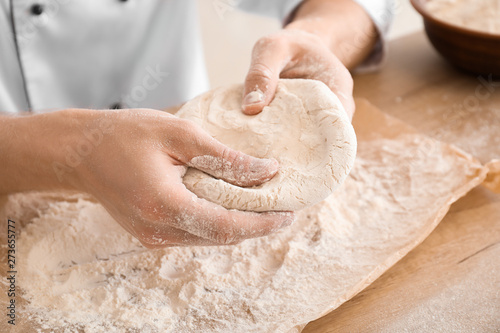 Male chef with raw dough in kitchen, closeup