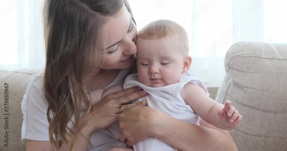 Happy mother kissing her cute baby daughter on sofa at home Happy mother kissing her cute baby daughter on sofa at home
