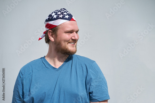 Portrait of young caucasian smiling man with USA flag bandana covered obove his head