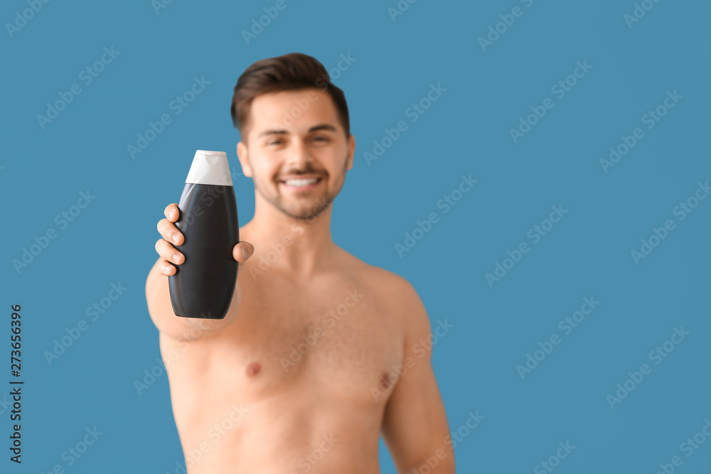 Fototapeta premium Handsome man with bottle of shampoo on color background