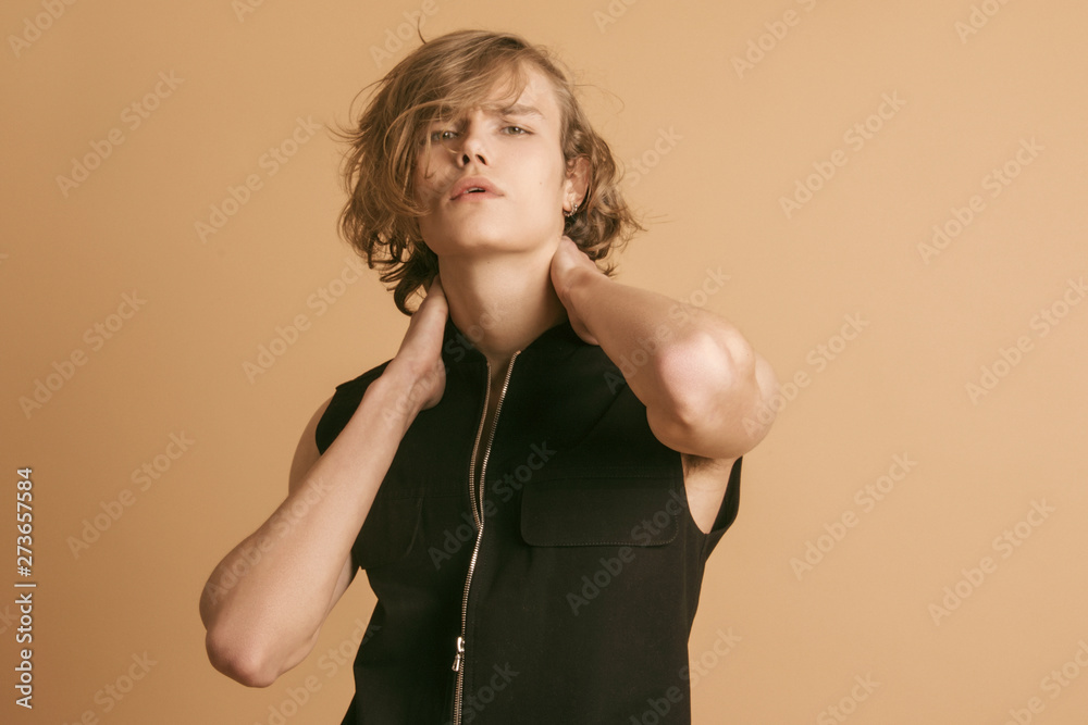 Muscle blonde beautiful stripped male model with long hair in black casual look on beige brown isolated font background Muscle blonde beautiful stripped male model with long hair in black casual look on beige brown isolated font background