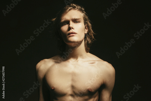 Muscle blonde beautiful stripped male model with long hair portrait in water drops on black isolated font background