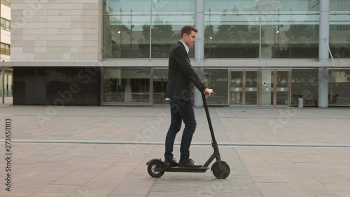 Young businessman riding an electric scooter for a business meeting in the office, office buildings, business man, sunset, electric transport, ecological transport, 4k, e-skateboard