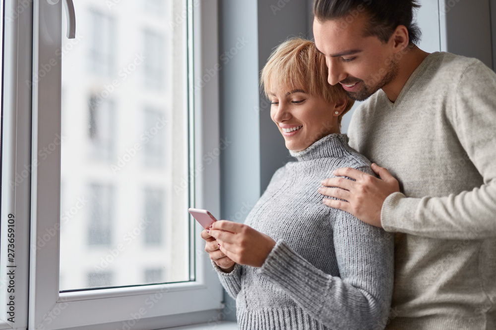 Fototapeta premium Couple using smartphone near window