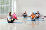 Elderly people practicing yoga with instructor in gym