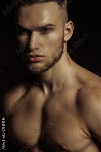 Handsome sport sexy stripped guy portrait in water drops on isolated black background