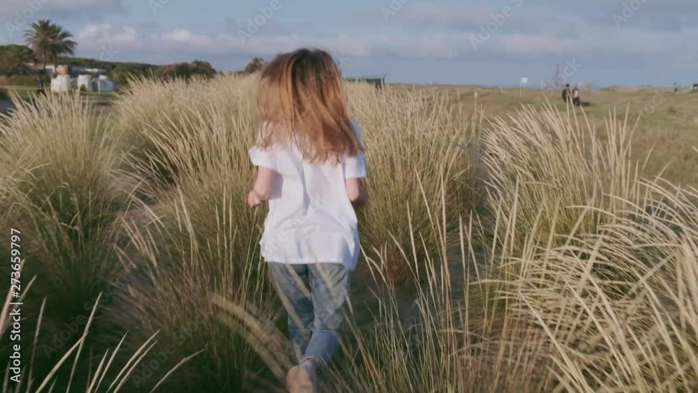 Cheerful young girl smiling and having fun running among the grass in a field near the beach Cheerful young girl smiling and having fun running among the grass in a field near the beach