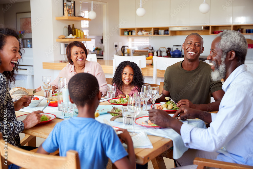 Multi-Generation Family Sitting Around Table At Home Enjoying Meal Together Multi-Generation Family Sitting Around Table At Home Enjoying Meal Together