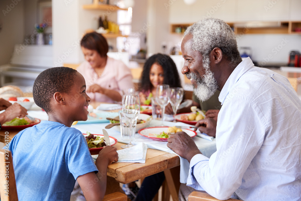 Multi-Generation Family Sitting Around Table At Home Enjoying Meal Together