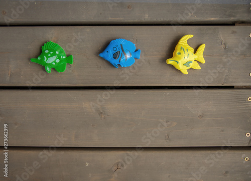 Three different toy fishes of green, blue and yellow colours on the wooden floor of a wooden country house. Horizontal orientation, space for text