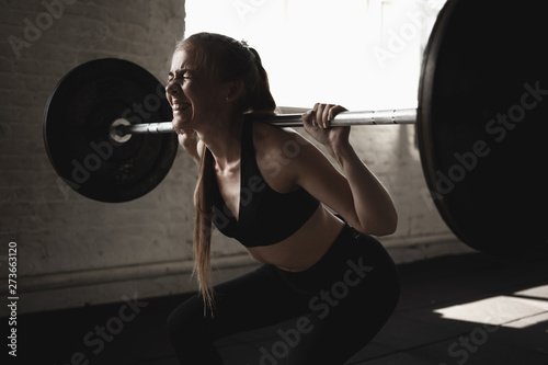 Fit young girl doing squats with barbell. Cross training workout.