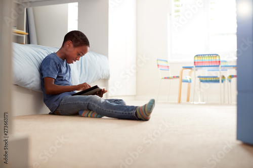 Boy Sitting On Floor In Bedroom Using Digital Tablet