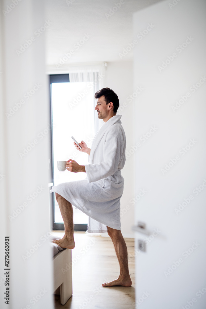 Young man with smartphone and coffee in the bedroom in the morning.