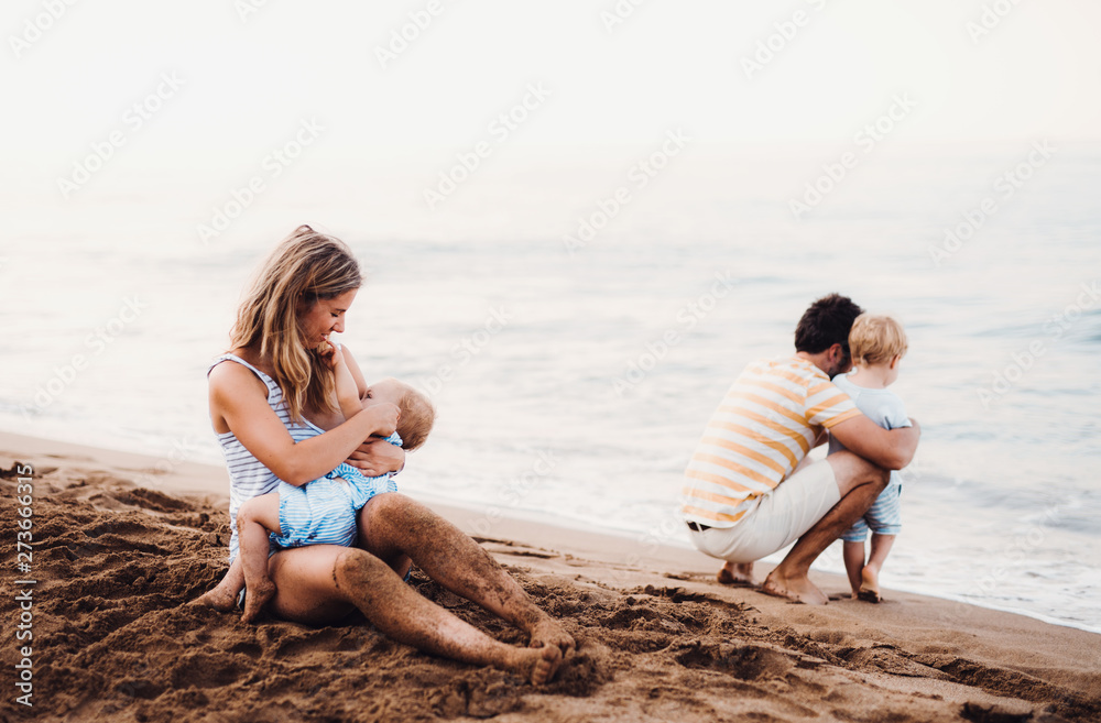 Young family with two toddler children on beach on summer holiday.
